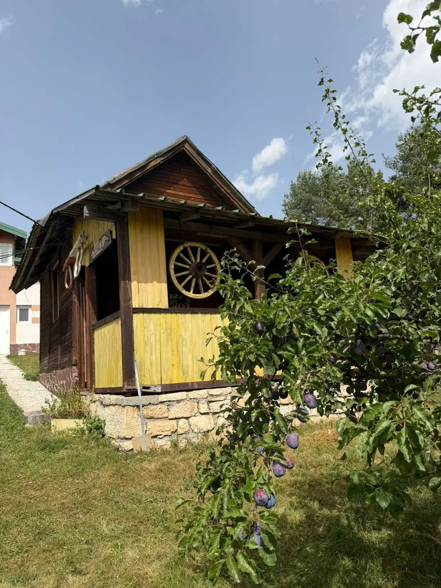Vikendica Sunce — žuta drvena kućica sa natkrivenom terasom pored šljive
