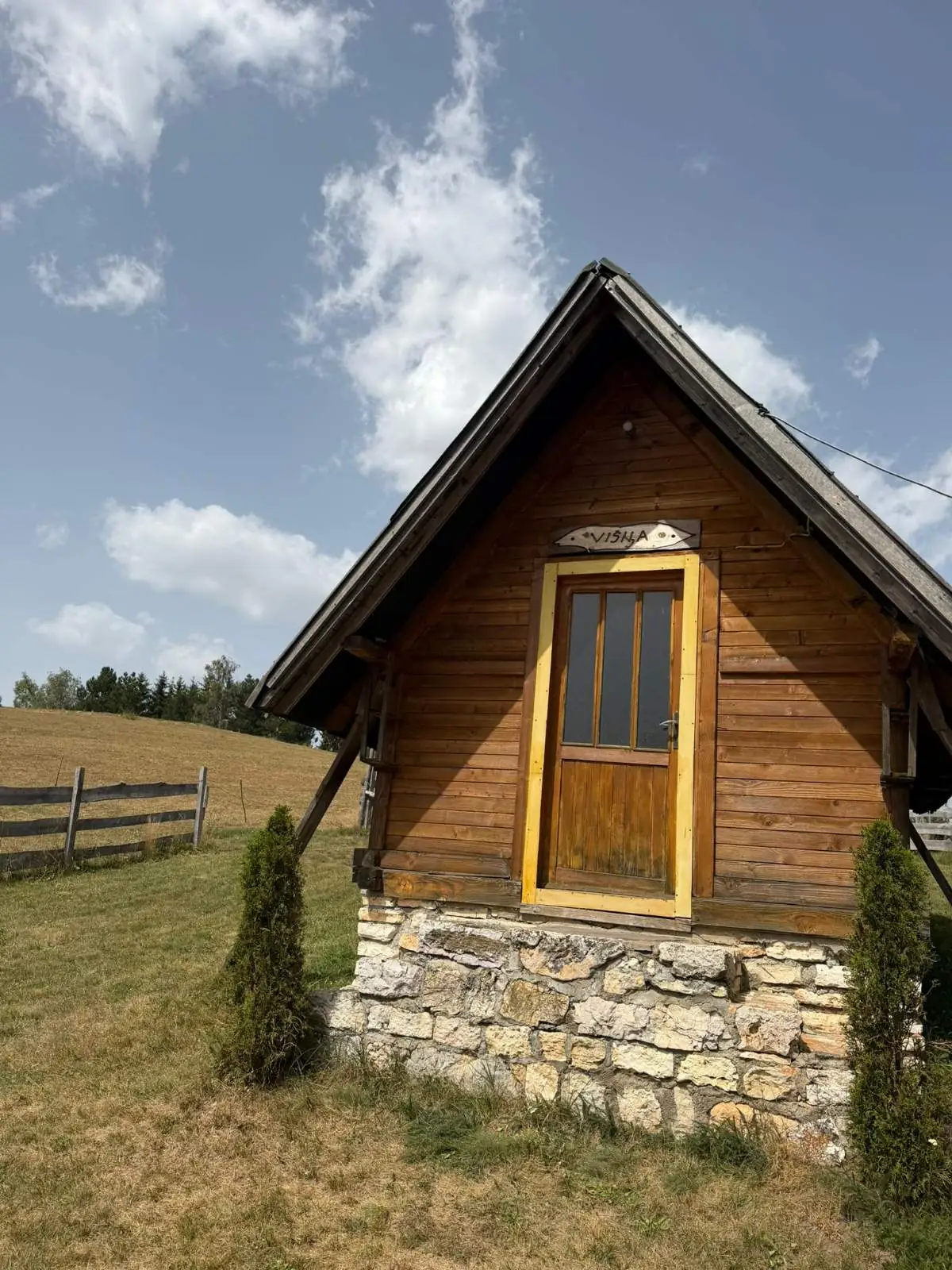 Vikendica Višnja — mala drvena kućica na kamenom postolju sa žutim ramom vrata